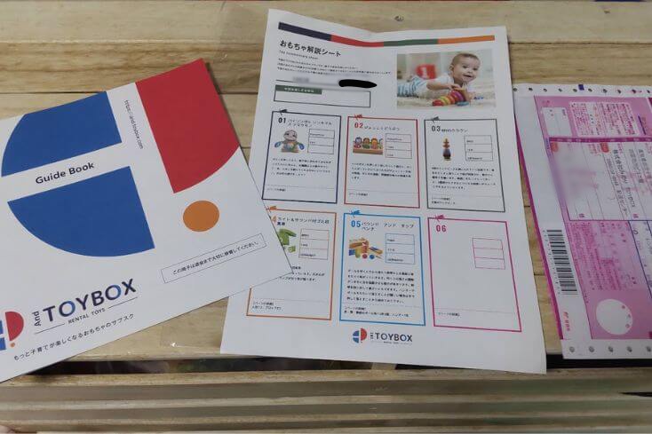 AndTOYBOX(アンドトイボックス)から届いたおもちゃの段ボールの中に入っていたガイドブックとおもちゃ解説シートと返却用の伝票の写真