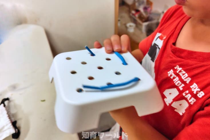 5歳の息子がジスターに付属している棒差しの土台でひも通しをして遊んでいるところの写真